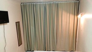 A room with a bed, a television mounted on the wall, and a curtain covering the window.
