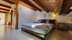 Ein Schlafzimmer mit einem Bett, Holzbalken an der Decke, einer weißen Tür und einem kleinen Nachttisch.