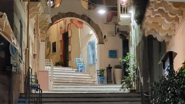 A nighttime view of a narrow street with a central archway leading to a building entrance. - Giuliana and Nino's Nest. (Carloforte)