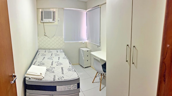 A small, well-lit bedroom with a bed, a desk, a wardrobe, and a window with blinds. - Vacanze - Barão de Mauá (Maceio)