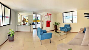A modern hotel lobby with a reception desk, seating area, and a view of the outside. - Vacanze - Barão de Mauá (Maceio)