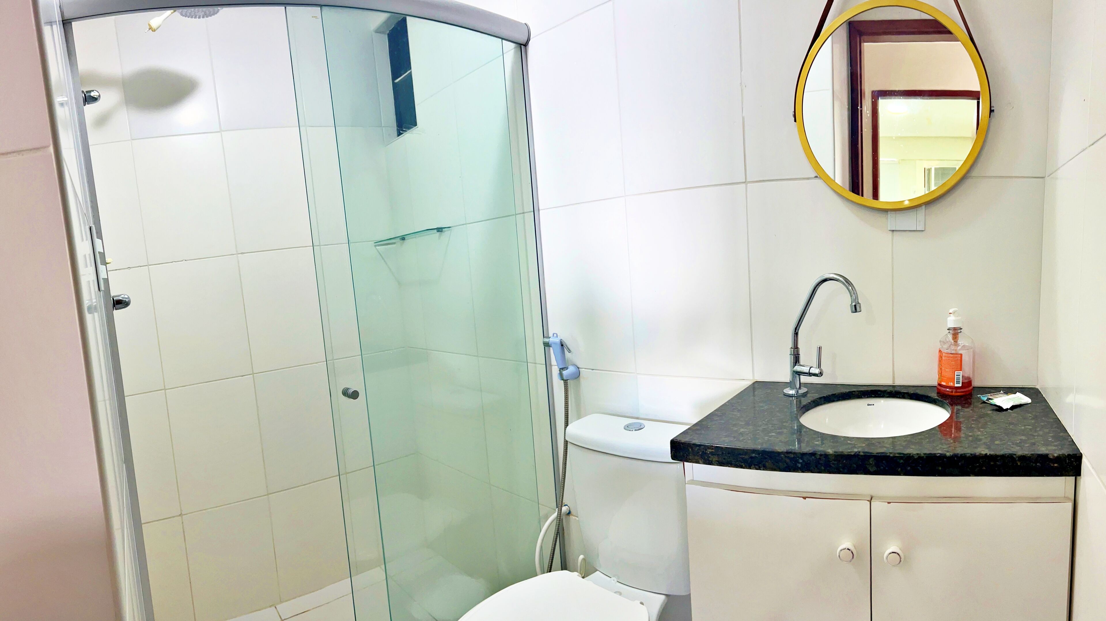 A modern bathroom with a glass-enclosed shower, a sink with a marble countertop, and a mirror with a gold frame.