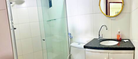 A modern bathroom with a glass-enclosed shower, a sink with a marble countertop, and a mirror with a gold frame.