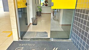 A hotel entrance with a glass door, a doormat with the hotel's name, a potted plant, and a trash bin. - Vacanze - Barão de Mauá (Maceio)