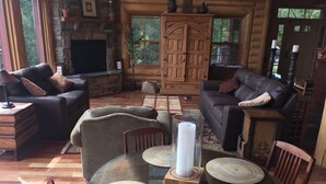 Een gezellig houten blokhut interieur met een stenen open haard, leren banken, een eettafel met houten plaatskaarten en een grote houten deur.