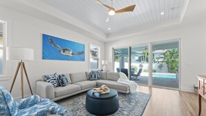 Una sala de estar moderna con un sofá modular, un otoman redondo y un cuadro grande de una tortuga marina.