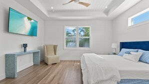Un dormitorio con una cama, un televisor en la pared, una ventana y un ventilador de techo.