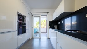 Una cocina moderna con armarios blancos, encimera negra y puerta corredera de vidrio que da a un balcón.