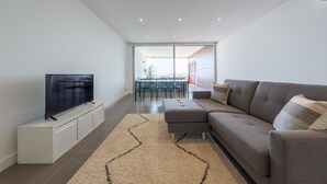 Una sala de estar moderna con un televisor de pantalla plana sobre un soporte blanco, un sofá gris con cojines y una alfombra beige con diseño en zigzag.