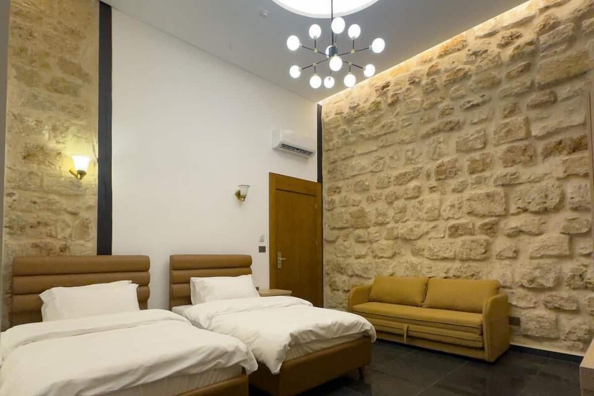 Ein modernes Schlafzimmer mit zwei Betten, einer Wand aus Stein, einer runden Deckenleuchte und einem Sofa.
