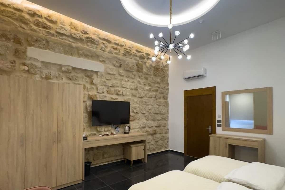 Ein Schlafzimmer mit Steinsandsteinwand, Fernseher, Schreibtisch, Bett, Spiegel und einer Deckenleuchte.