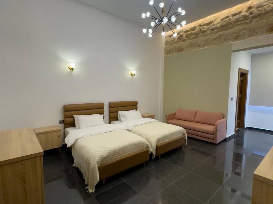 A modern bedroom with a large bed, a wooden nightstand, a pink sofa, and a unique ceiling light fixture.