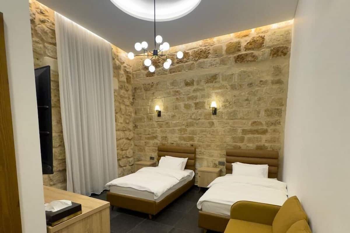 Ein modernes Hotelzimmer mit zwei Betten, einem Holztisch, einer Couch, Steinwänden und einer außergewöhnlichen Deckenleuchte.
