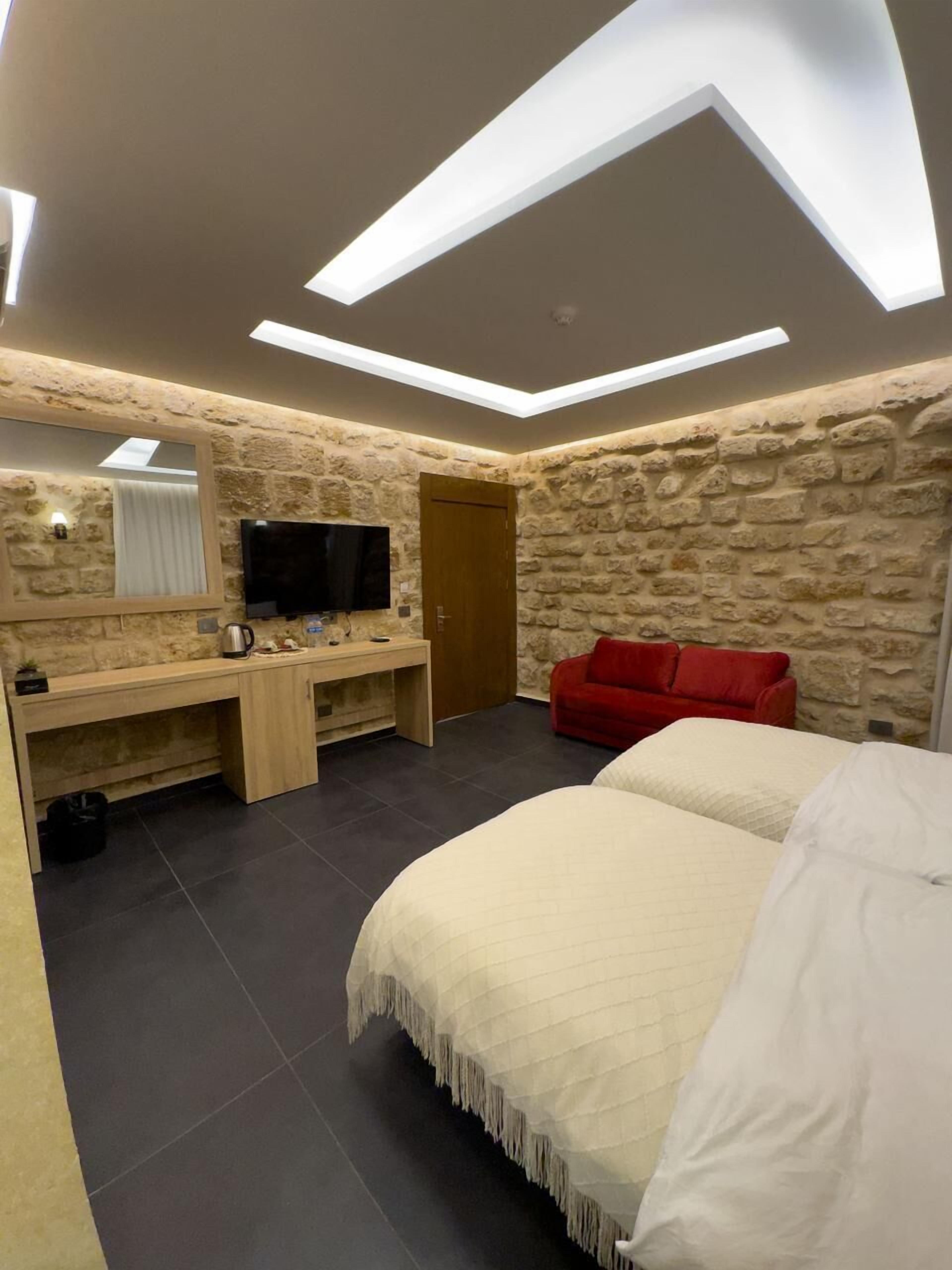 Un dormitorio con cama, televisor, escritorio y sofá rojo.