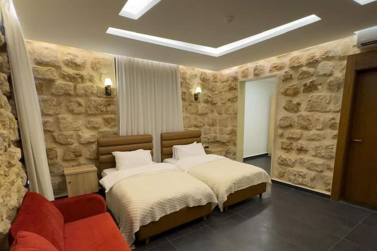 Ein Schlafzimmer mit zwei Betten, einem roten Sofa, Steinwänden und eingelassener Deckenbeleuchtung.