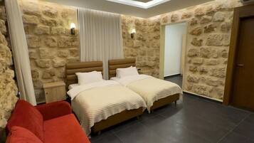 A bedroom with two beds, a red sofa, stone walls, and recessed ceiling lighting.
