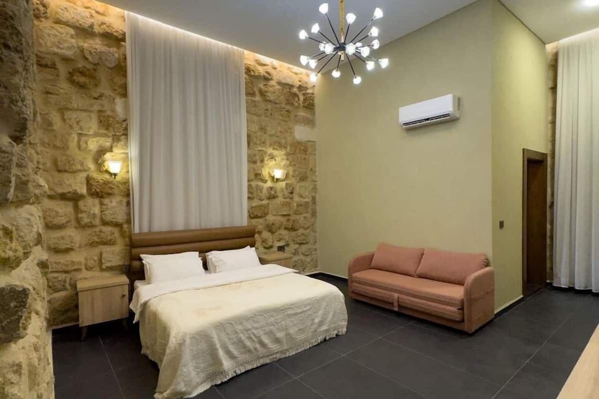 Ein Schlafzimmer mit Steinwand, einem Bett mit weißen Leinen, einem rosafarbenen Sofa und einer modernen Chandelier.