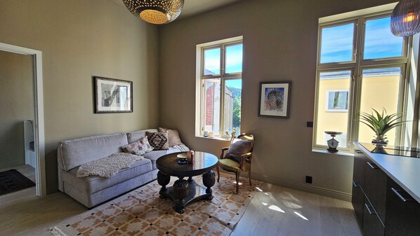 A living room with a sofa, a round coffee table, a chair, and a window with a view of a building.