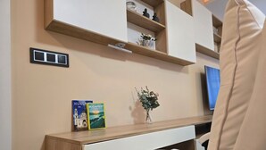 A modern office chair with a high backrest and armrests, positioned next to a desk with a wooden finish. On the desk, there are two books titled 'Hungary' and 'Budapest', a small vase with green foliage, and a wall-mounted shelf with decorative items.