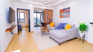 A modern living room with a grey sofa, a coffee table, a TV mounted on the wall, and a large window with curtains.