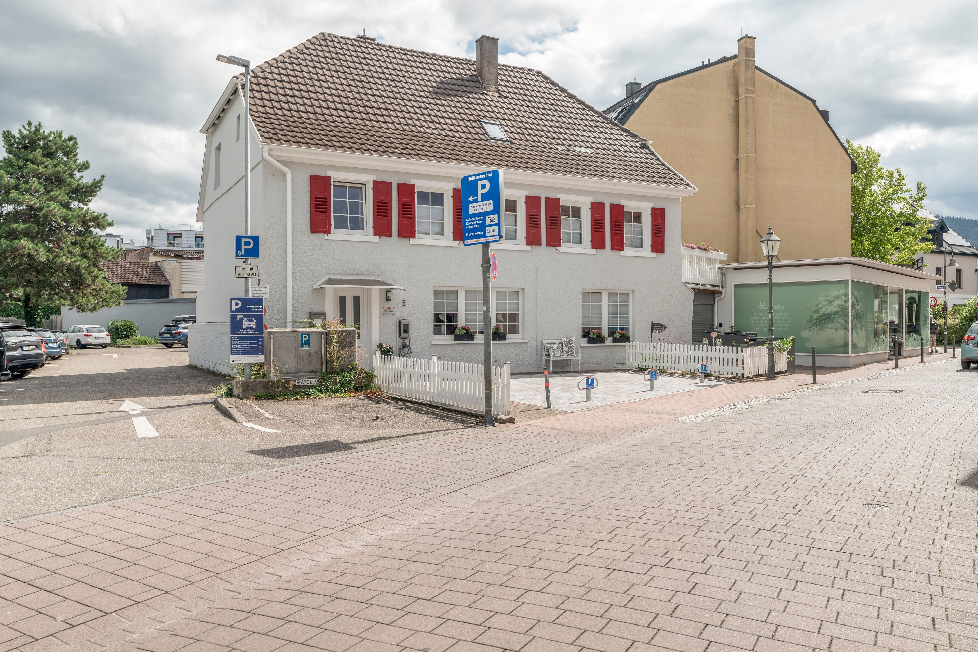 Ein weißes Gebäude mit roten Fensterläden, einem Parkplatzschild und einem weißen Zaun.