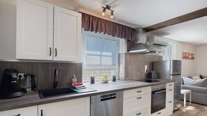 A modern kitchen with white cabinets, stainless steel appliances, a dishwasher, and a window with blinds.