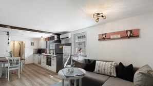A modern kitchen with white cabinets, a dining area with a table and chairs, and a living room with a sofa and cushions.