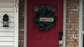 Eine rote Tür mit einem 'WELCOME'-Schild, einem Briefkasten und der Hausnummer 2201.