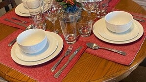 Ein Esszimmertisch mit weißen Tellern, Schüsseln und Besteck, umgeben von Stühlen.