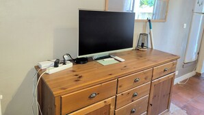 A wooden dresser with a flat-screen TV, a lamp, and a remote control on top.