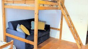 A room with a bunk bed, a sofa, a chair, and a ladder.