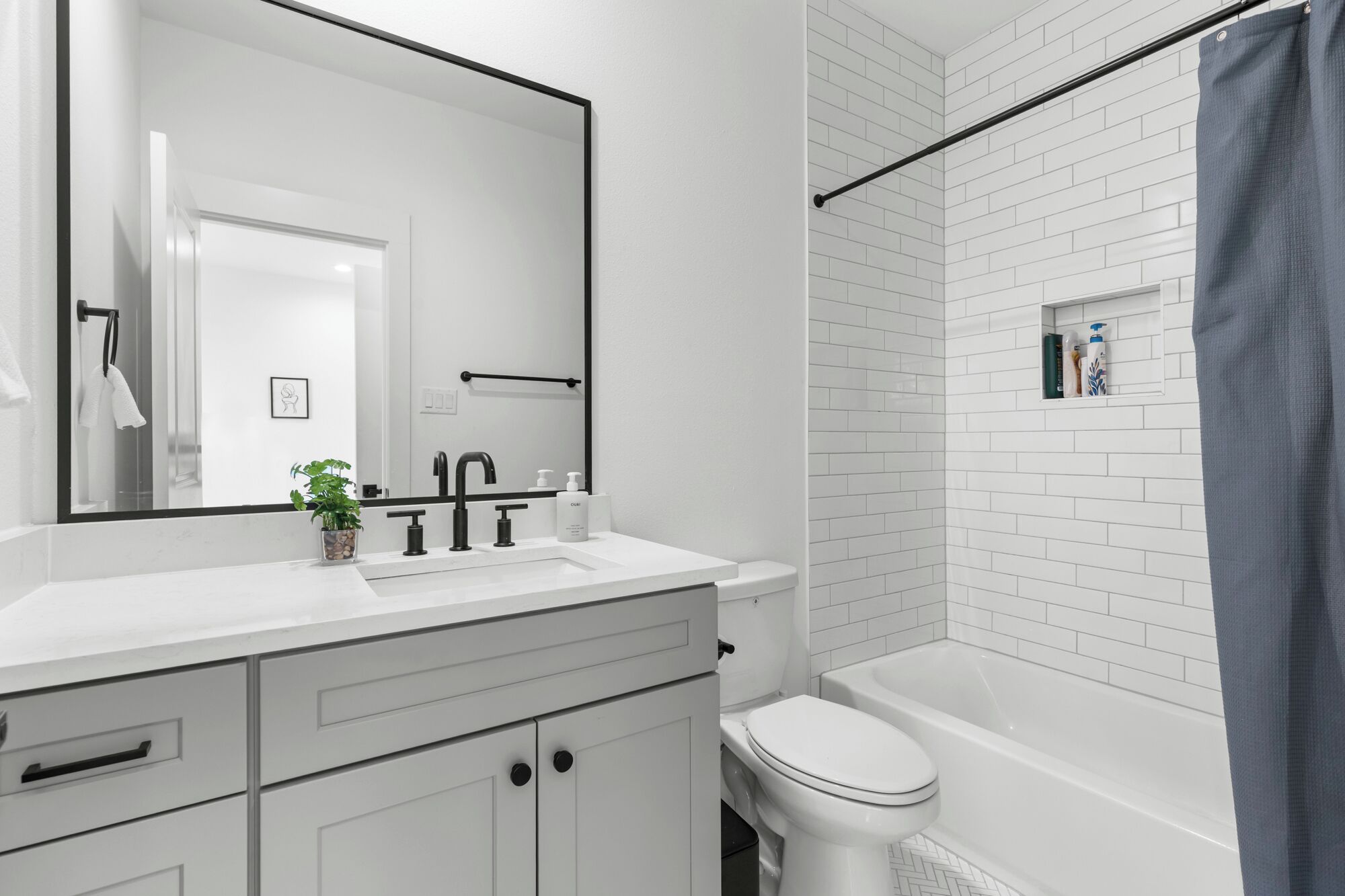 Une salle de bain moderne avec des carreaux blancs, un grand miroir, un lavabo blanc, des toilettes et une baignoire.
