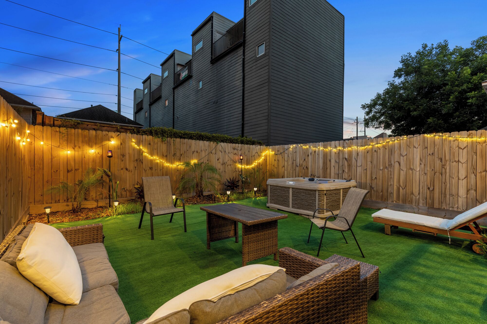 A backyard with a hot tub, wicker furniture, and a wooden fence.