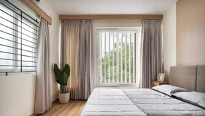 Quarto com uma cama grande, uma planta em vaso e uma janela com cortinas.