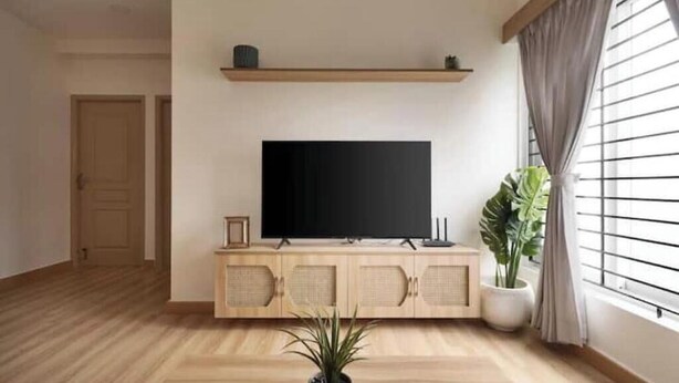Uma sala de estar com televisão de tela plana em um móvel de madeira, um vaso de planta e uma janela com persianas.