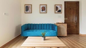 Quarto com sofá azul, mesa de madeira e três obras de arte emolduradas na parede.