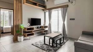 A modern living room with a flat-screen TV, wooden shelving, a coffee table, and a potted plant.