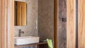 A modern bathroom with a marble wall, a wooden door, and a white sink.