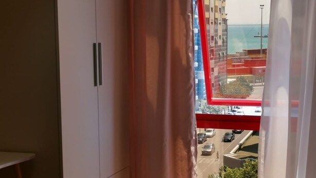Ein Zimmer mit großem Fenster, Kleiderschrank und Blick auf ein Gebäude sowie eine Straße.