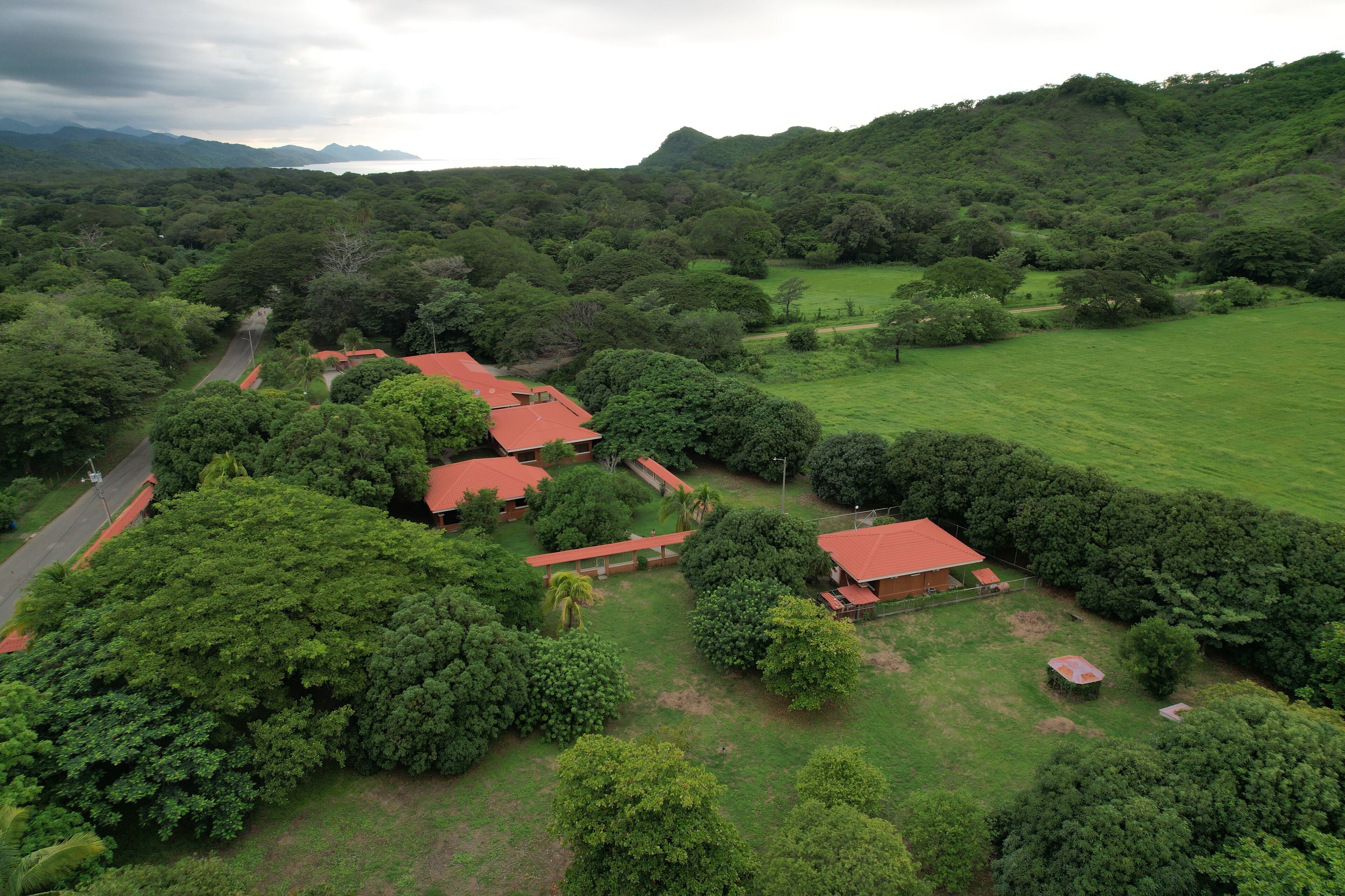 An aerial view of a property with multiple red-roofed buildings surrounded by lush greenery and hills.