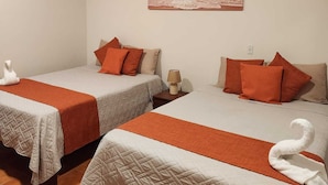 Een hotelkamer met twee bedden, elk voorzien van een gewatteerde spreideken en kussens, een schilderij van een zonsondergang aan de muur, en een zwaan handdoek op elk bed.