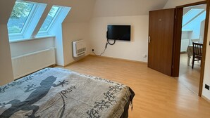 A bedroom with a bed, a TV mounted on the wall, a radiator, and a door leading to another room. - Cozy vacation apartment on the edge of the forest - ideal for nature lovers & families (Bark)