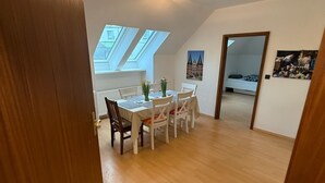 A dining area with a table and chairs, a skylight, and a bed in the background. - Cozy vacation apartment on the edge of the forest - ideal for nature lovers & families (Bark)