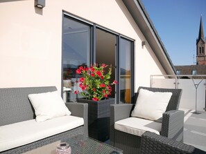 Un balcon agrémenté de meubles en osier, d’une table en verre et d’une plante en pot.