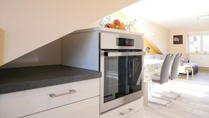 A kitchen with a built-in oven, a dining area with a table and chairs, and a window with a view. - Apartment 'Kirschblüte' (Achern)