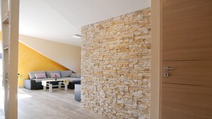A modern living room with a stone accent wall, a wooden door, and a sofa with cushions. - Apartment 'Kirschblüte' (Achern)