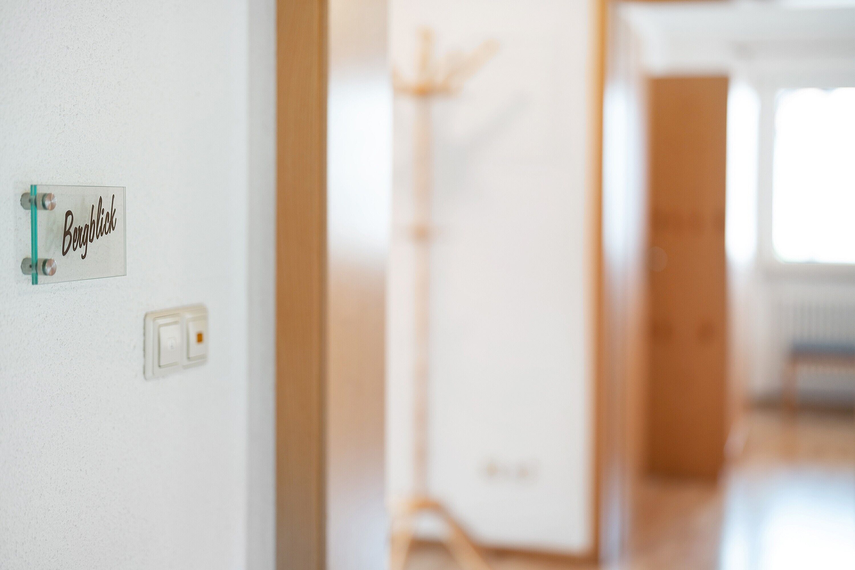 A sign with the word 'Bergblick' on a wall, a light switch, and a coat rack in the background.