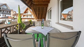 Un balcón con una mesa dispuesta para dos personas, una sombrilla verde y una botella de vino.