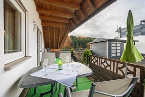 Un área de estar al aire libre con techo, una mesa preparada para dos, un banco y un paraguas verde.