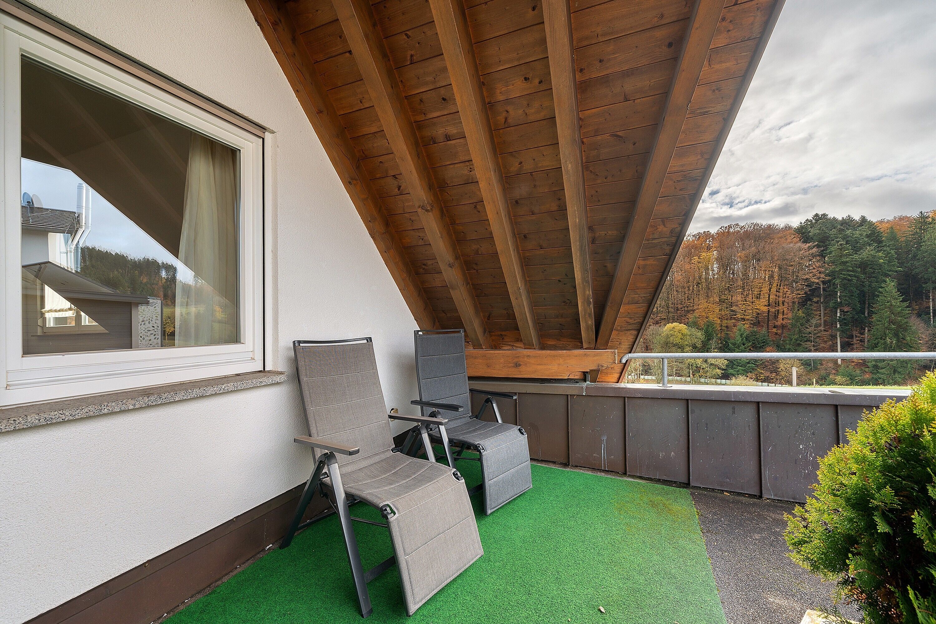 A balcony with a wooden ceiling, a window, and a view of trees.